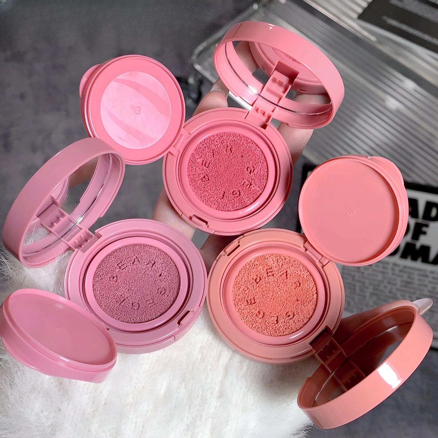 Pink makeup compacts with open lids on a textured surface