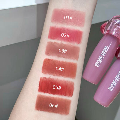 Lipstick swatches on a arm with a lip gloss tube labeled 'GEGE BEAR' in the background.