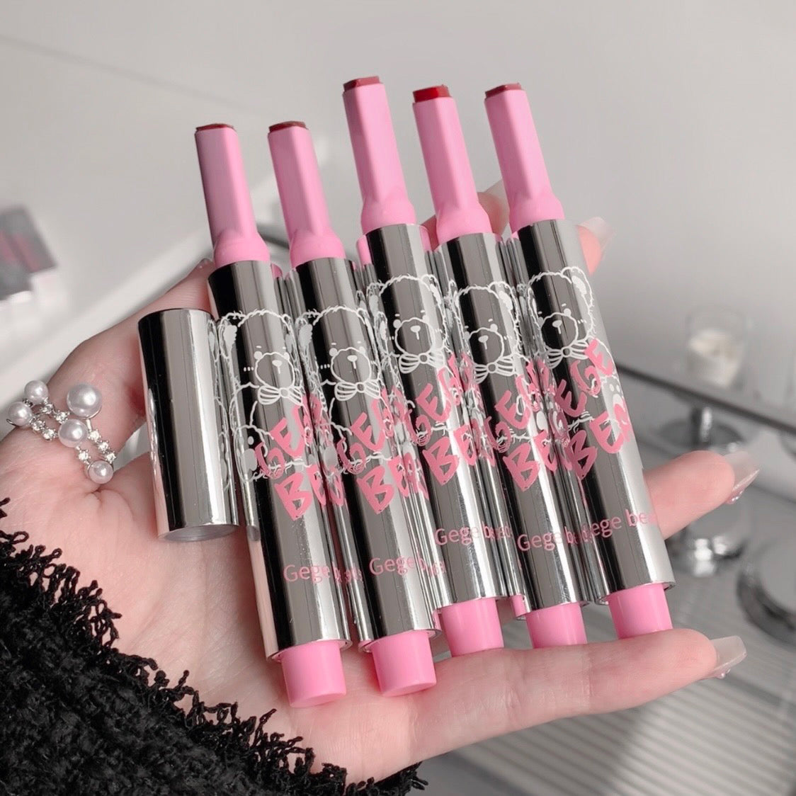 Set of pink and silver lip glosses held in a hand with a blurred background