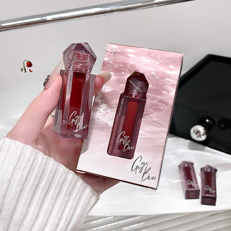 Red lip gloss with a matching box held by a hand, on a white surface.