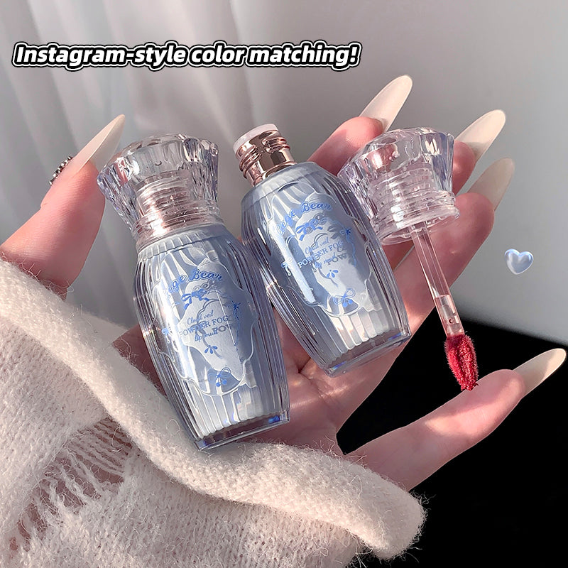Lip gloss set with clear and blue bottles held by a hand against a neutral background.
