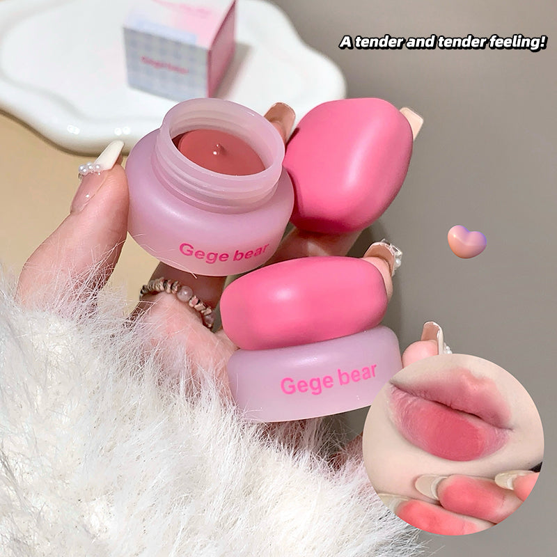 Pink lip balm and container held by a hand with a soft focus background