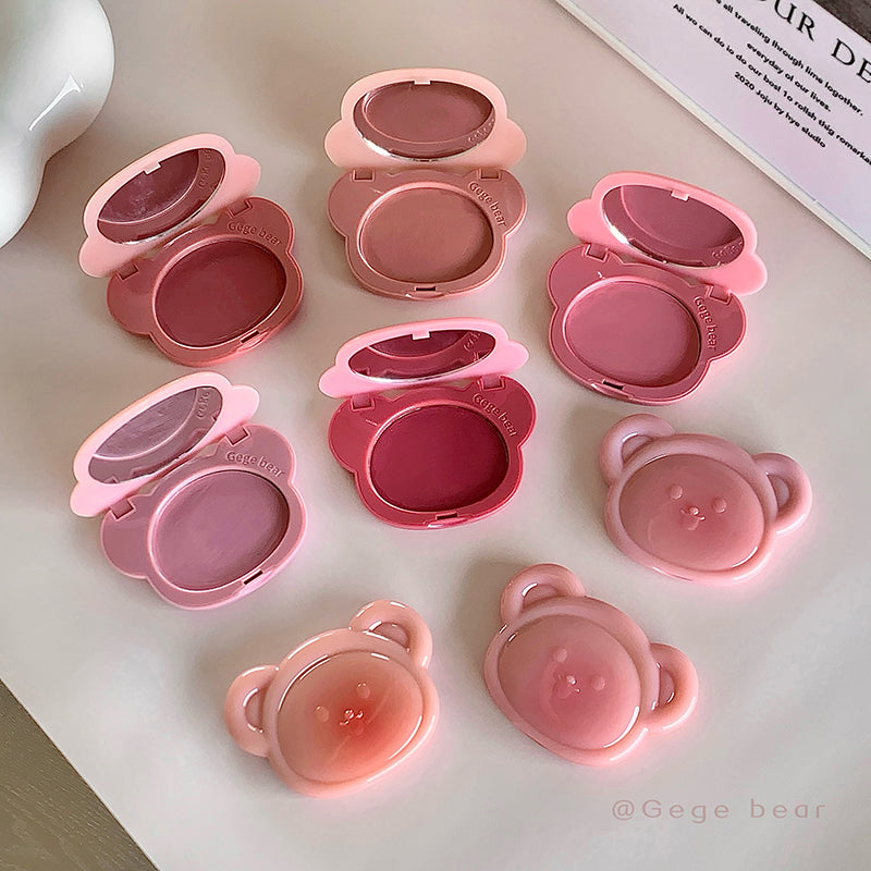 Set of pink makeup products with bear-shaped caps on a light surface.