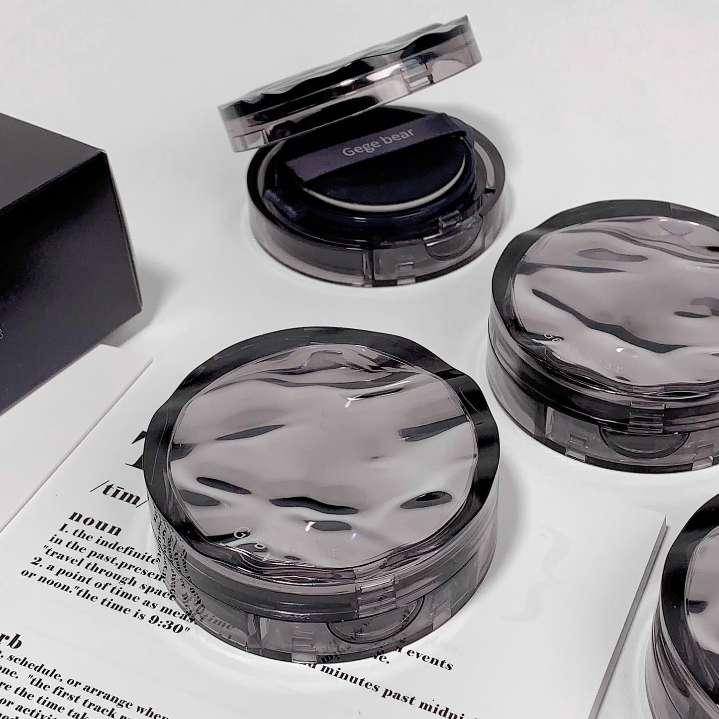Compact cosmetic cases with 'Gege bear' branding on a white surface.