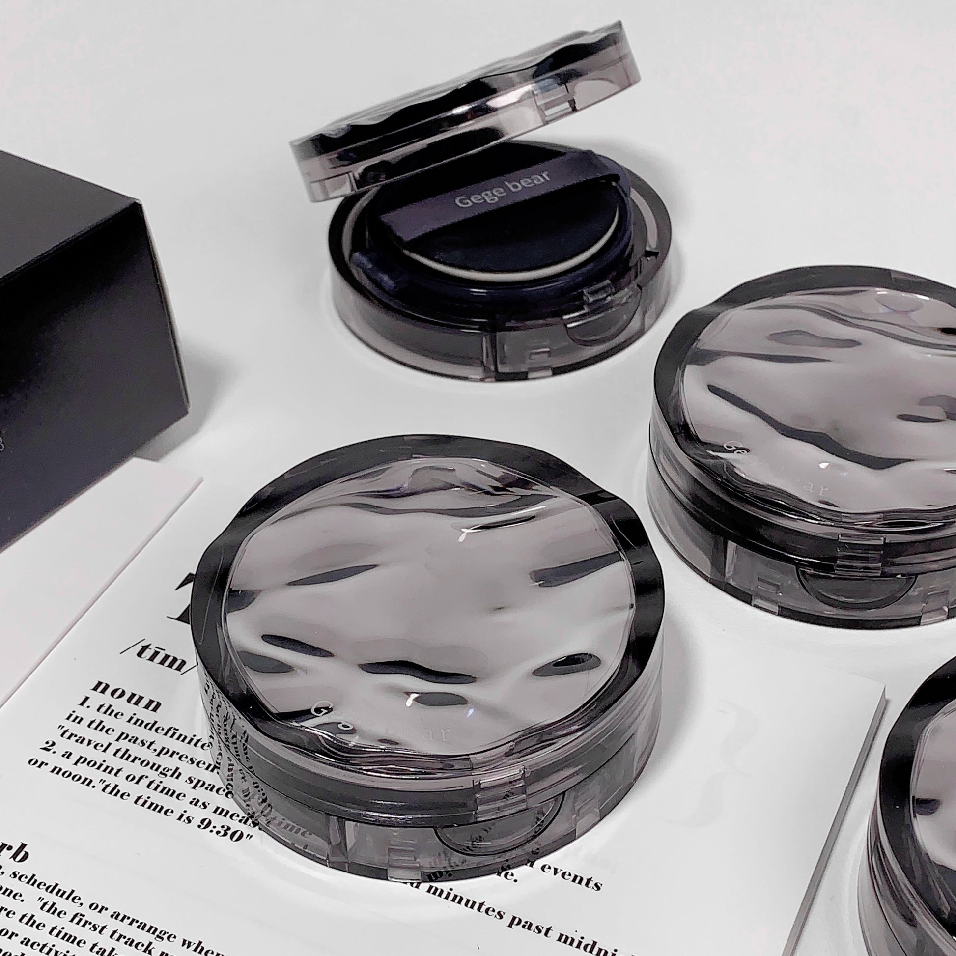 Compact cosmetic cases with 'Gege bear' branding on a white surface.