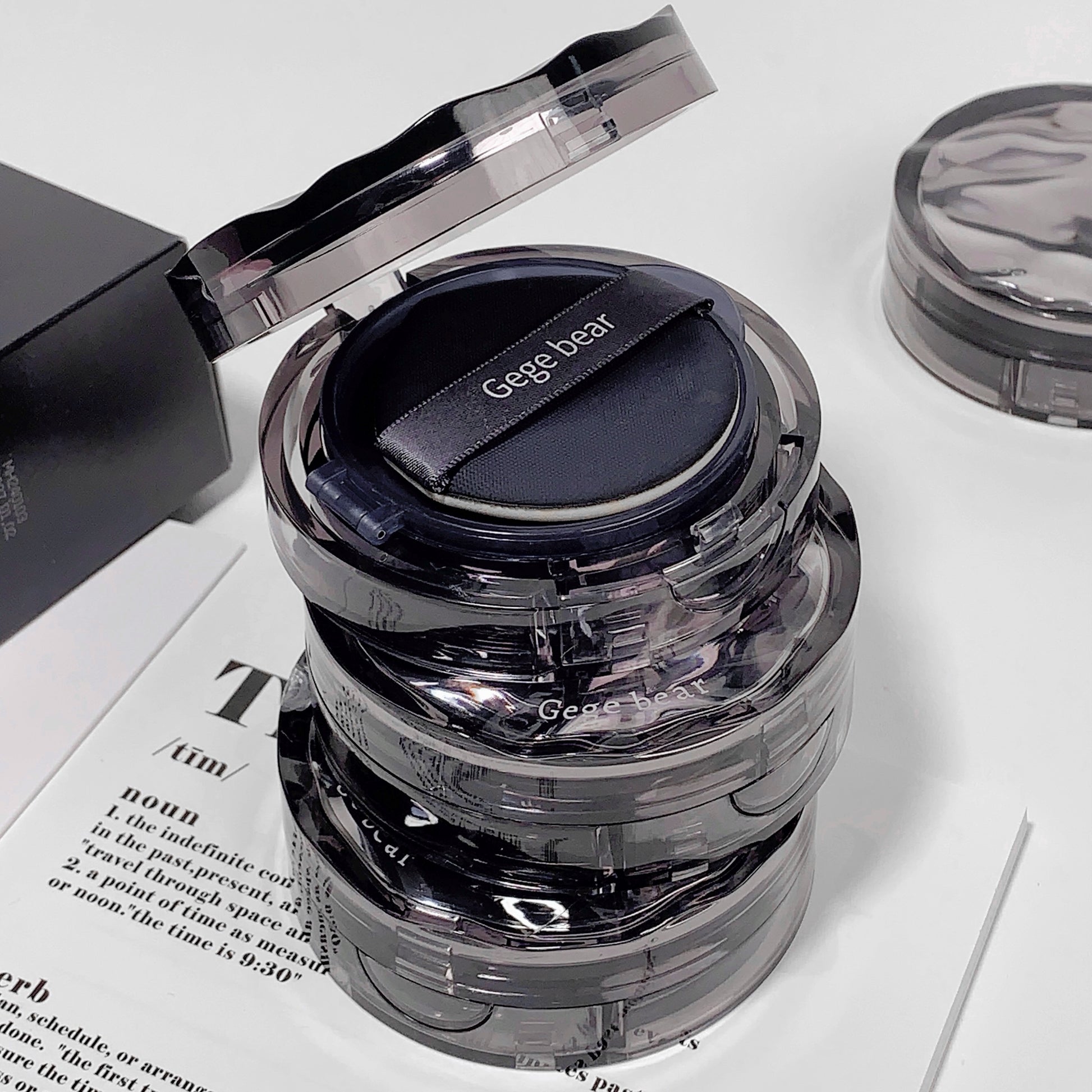 Cosmetic compact with 'Gegebear' branding on a white surface with newspaper.
