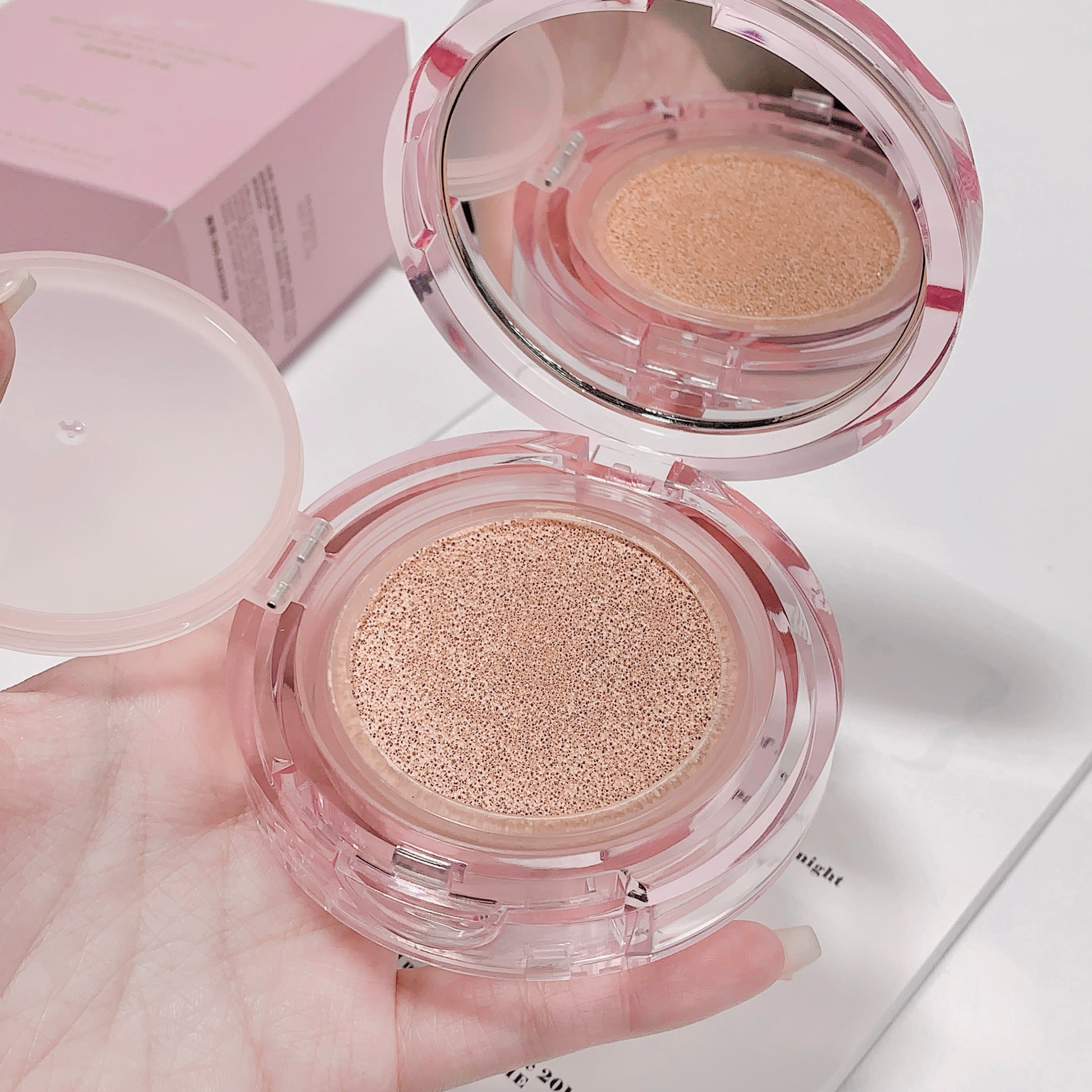 Compact powder in a clear case held by a hand on a light background