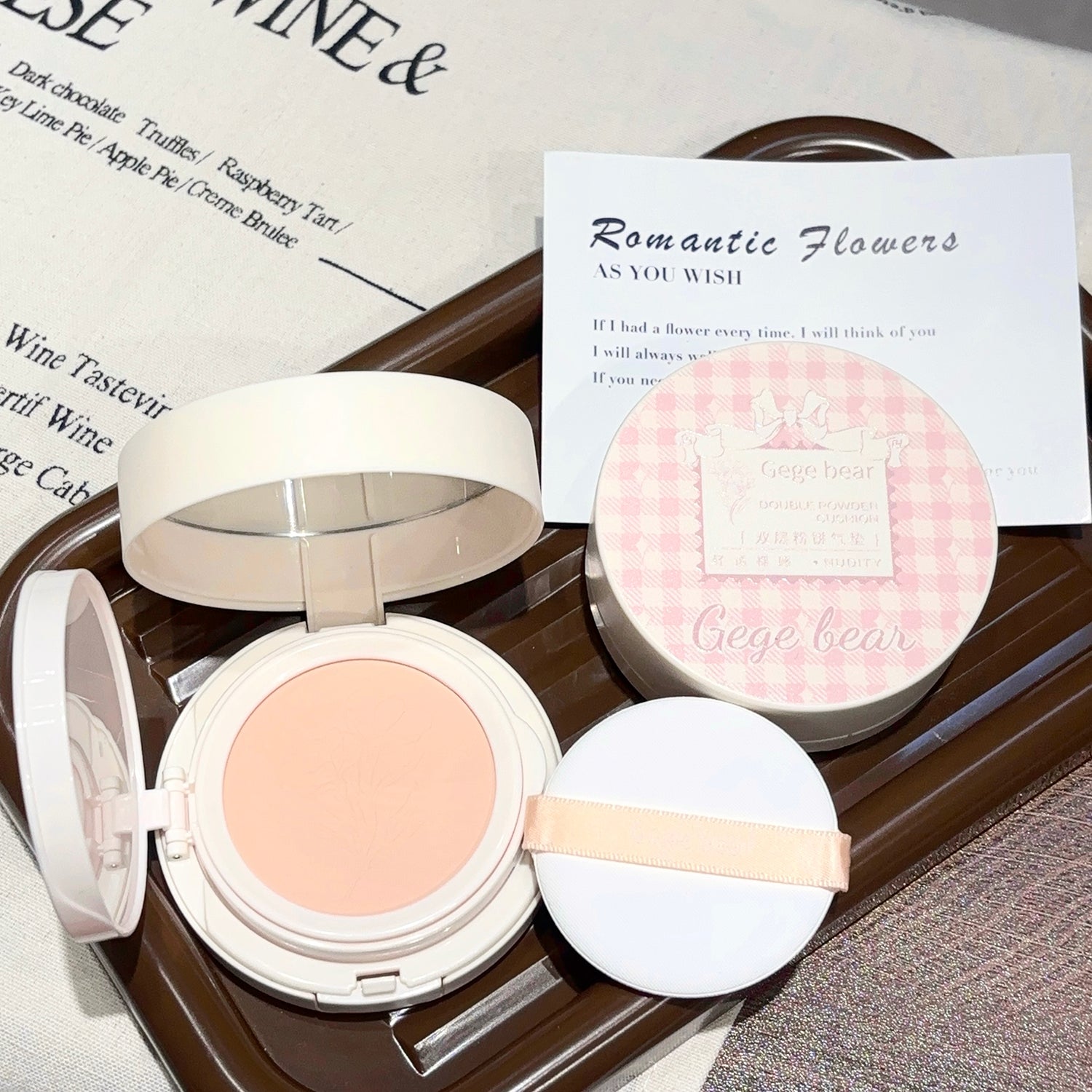 Compact powder with a pink blush on a tray with a card in the background