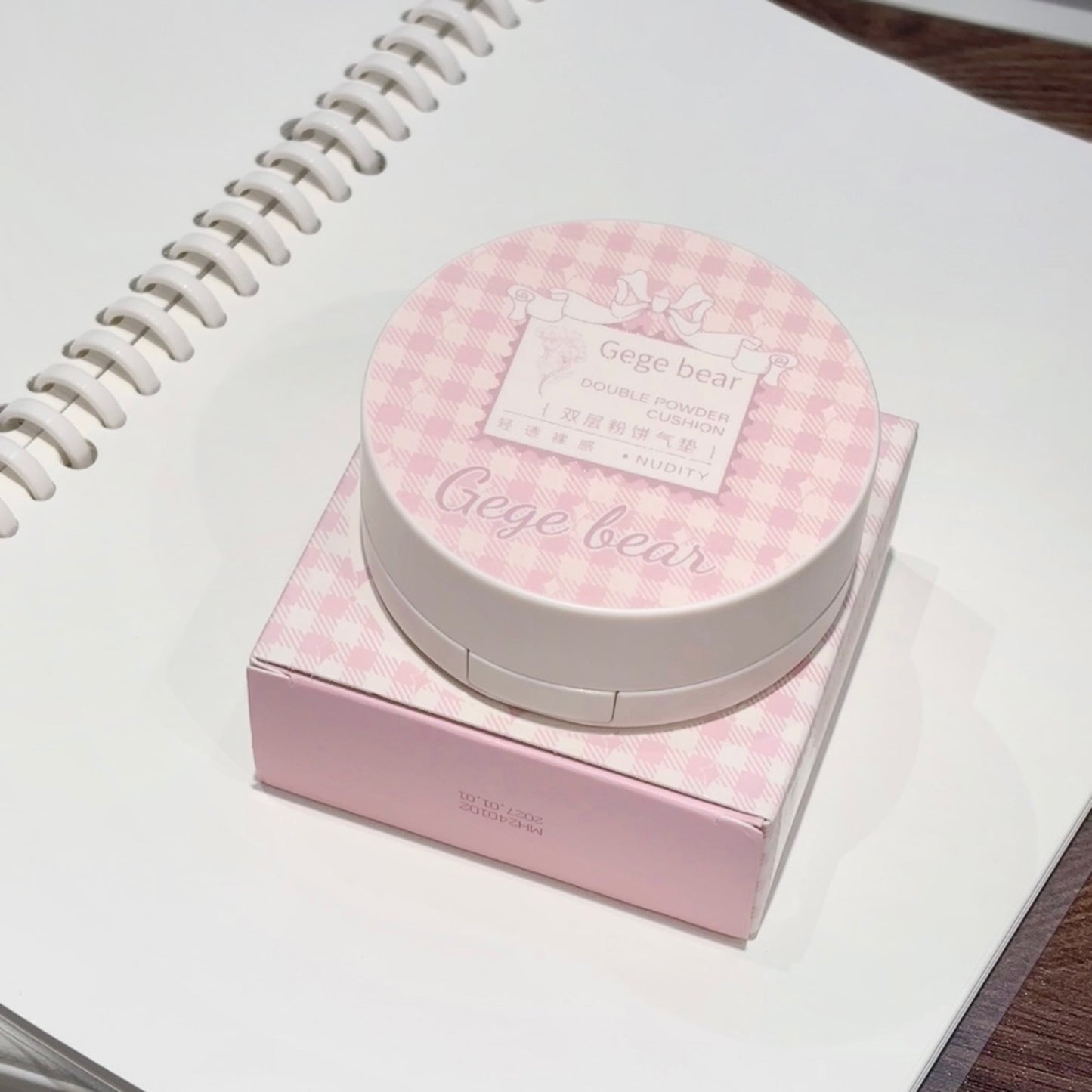 Pink checkered makeup compact and box on a white surface