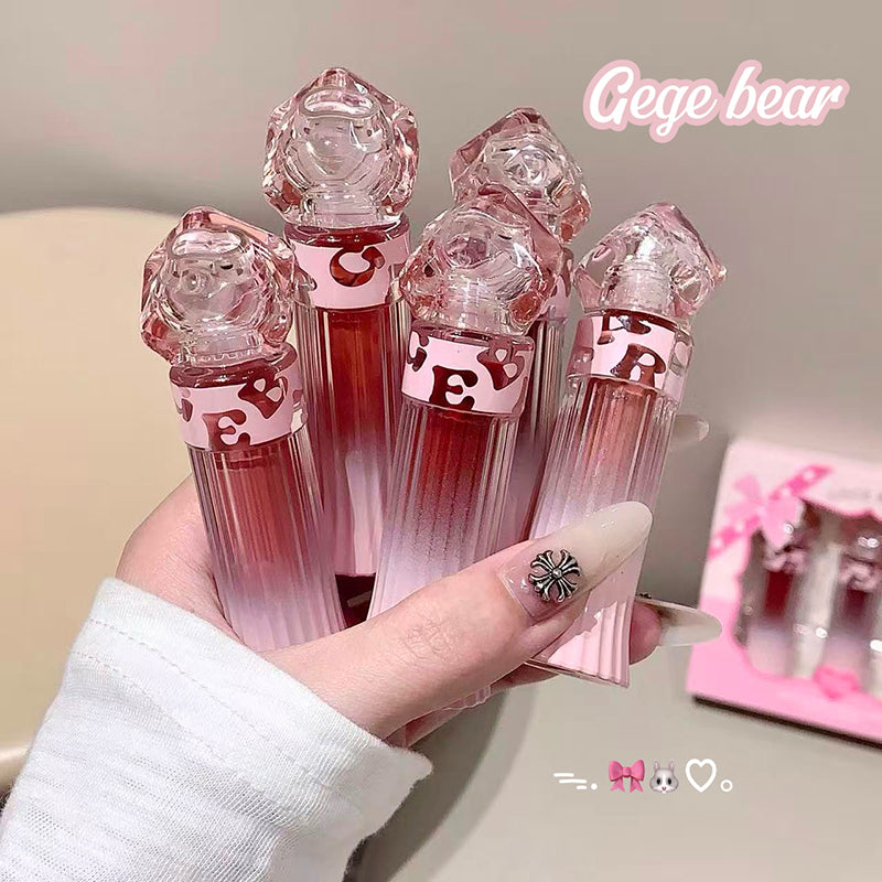 Set of pink lip glosses with geometric designs held by a hand, branded 'Gege bear'.