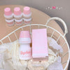 Pink and white cosmetic products including bottles and a box on a white wire basket.