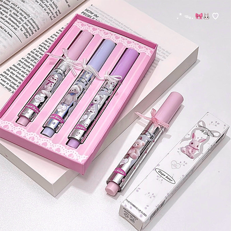Set of pink and purple lip balms with bunny designs in a decorative box on a white surface.