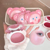 Pink makeup product with bear design held by a hand, displayed against a neutral background.