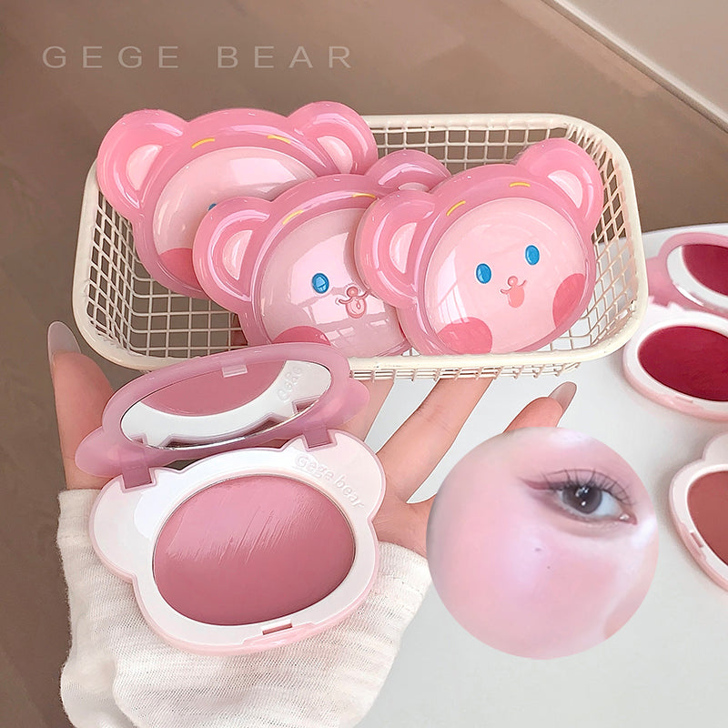 Pink makeup product with bear design held by a hand, displayed against a neutral background.
