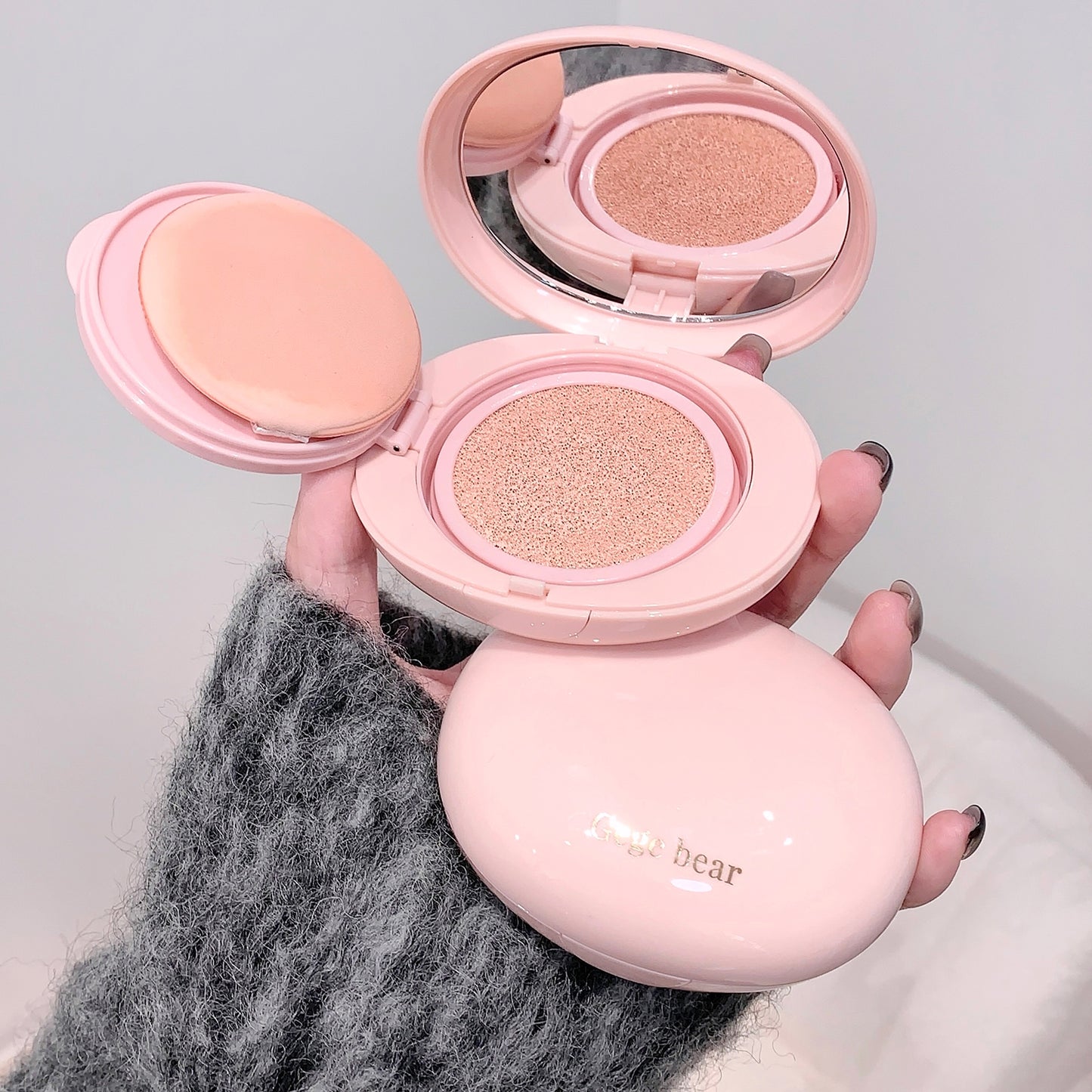 Pink cosmetic compact with two shades held by a hand against a neutral background