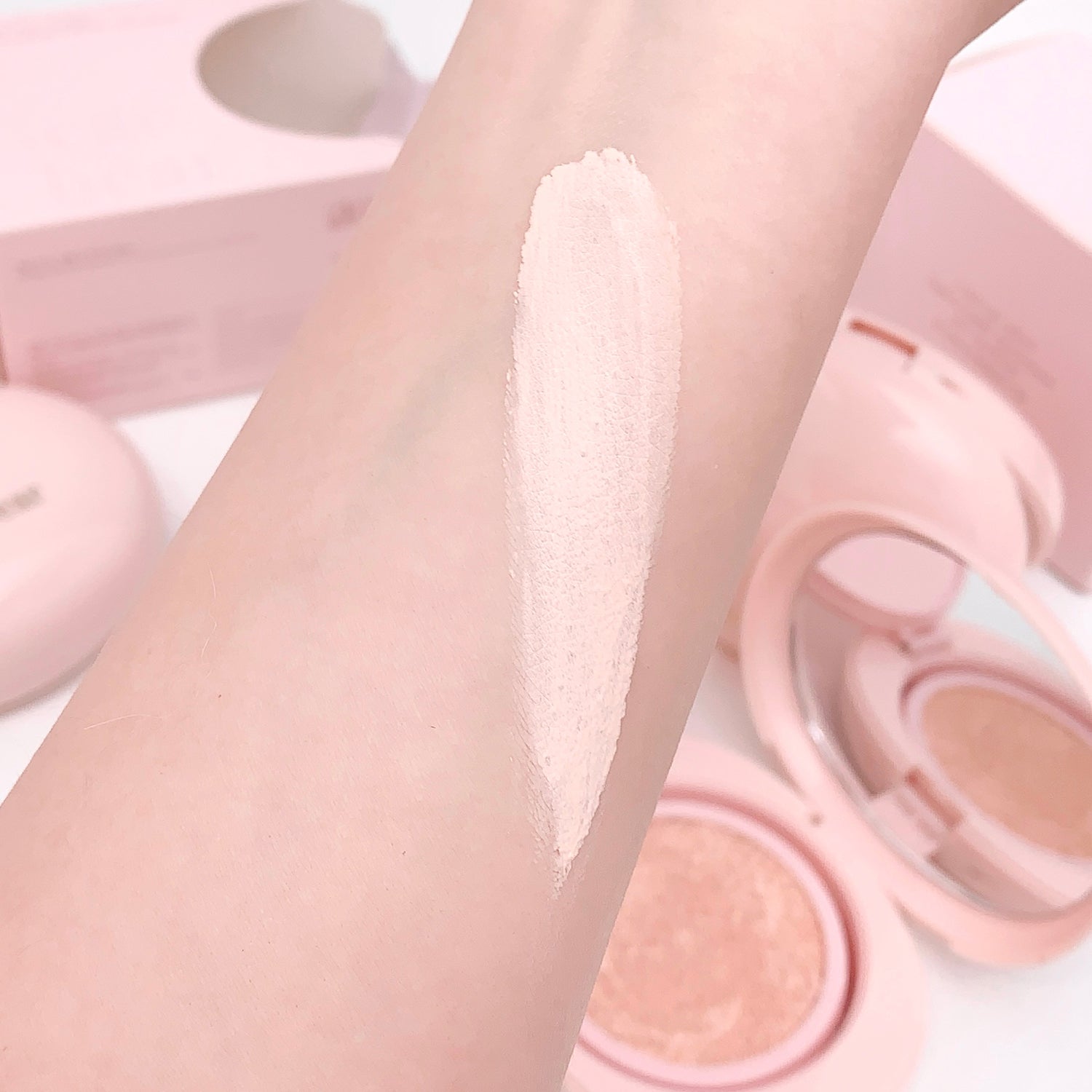 Cosmetic product swatch on skin with pink makeup items in the background