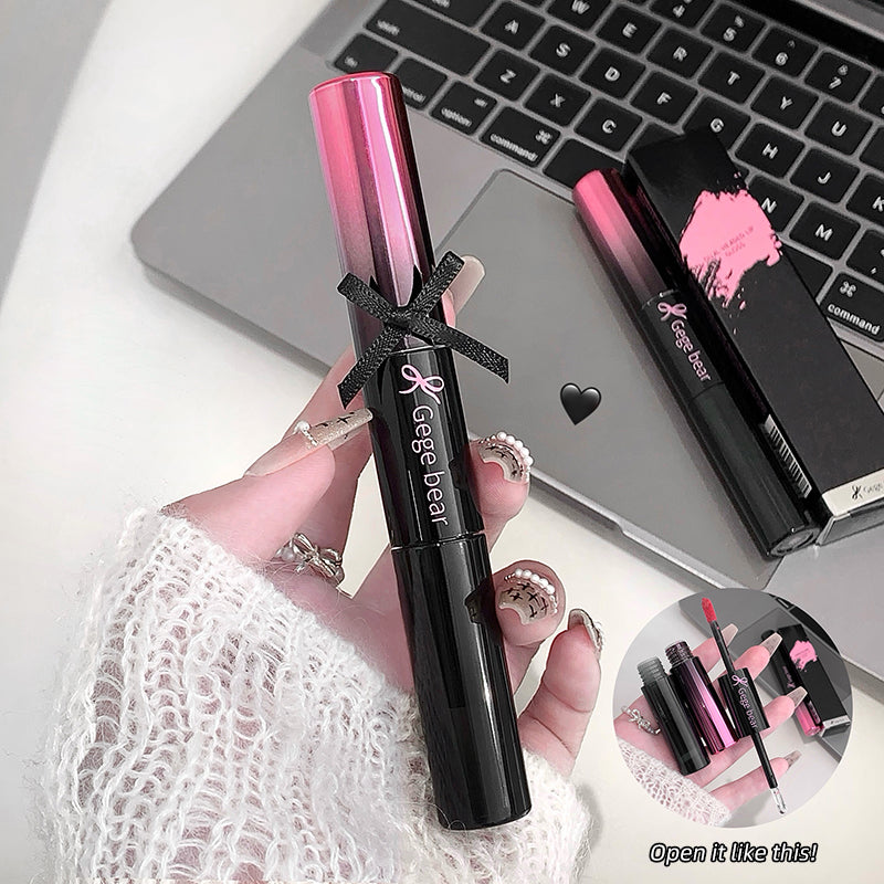 Hand holding a black and pink cosmetic product with a laptop in the background