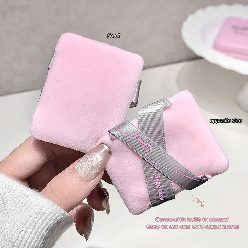 Pink plush toy with a gray ribbon held by a hand on a light background