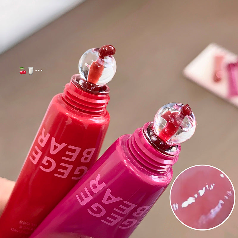 Two red lip gloss bottles with a close-up of the product on a neutral background