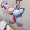 Two bear-shaped water bottles with keychains on a plain background