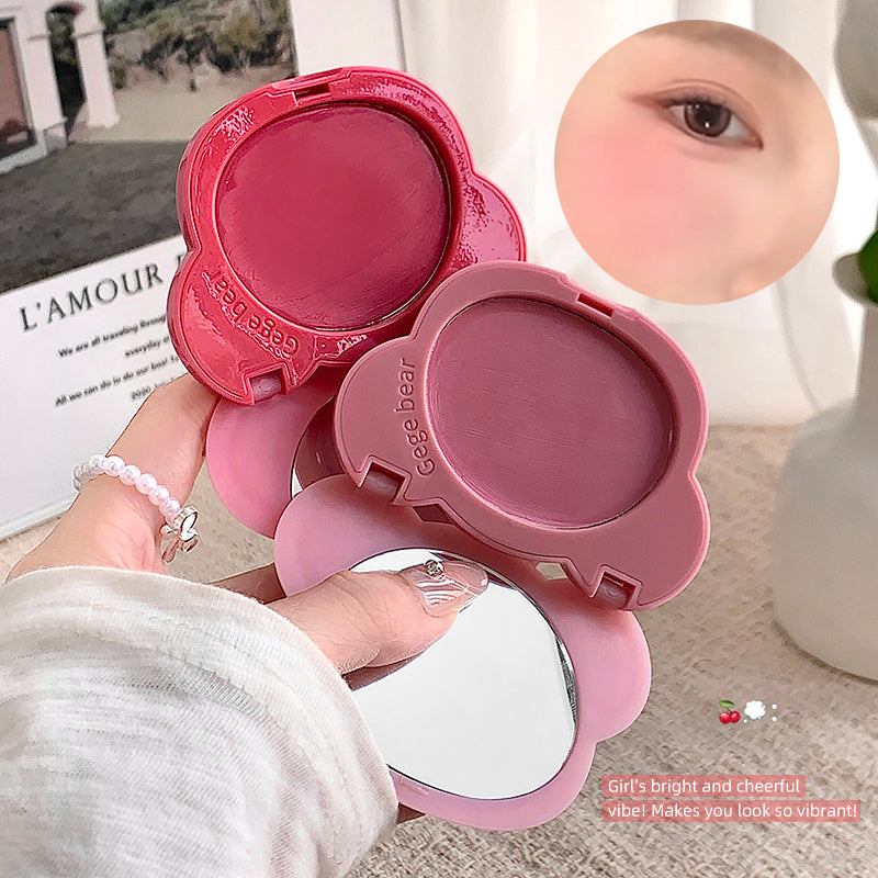 Pink makeup compact with a mirror held by a hand, with a blurred background.