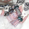 Multiple small nail polish bottles held in a hand with a mirror and decorative items in the background.