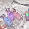 Three small perfume bottles in purple, pink, and blue on a decorative tray with a pearl necklace.