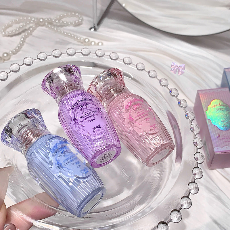 Three small perfume bottles in purple, pink, and blue on a decorative tray with a pearl necklace.