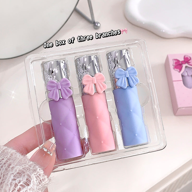 Three colorful lip glosses with bow decorations in a clear packaging on a light background.