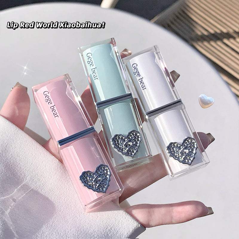 Three lip glosses with heart designs held by a hand on a light surface.