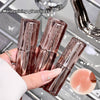 Three glass lip balm tubes held by a hand with a close-up of a lip balm on a reflective surface.