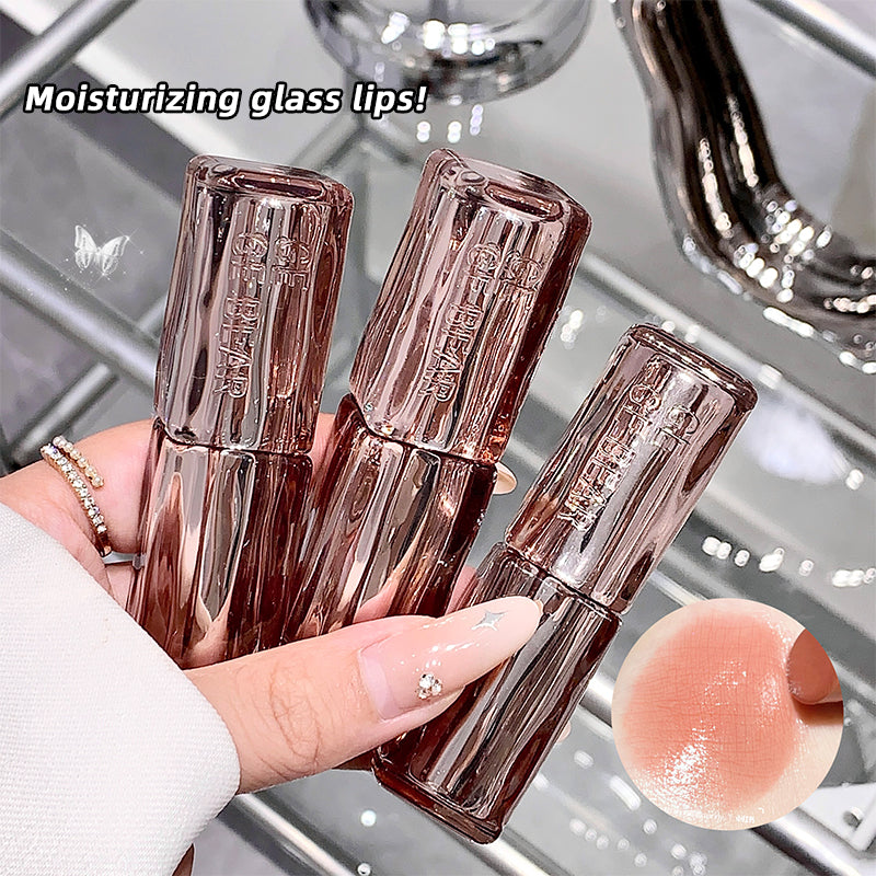 Three glass lip balm tubes held by a hand with a close-up of a lip balm on a reflective surface.