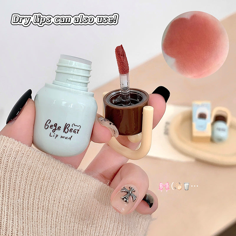 Lip mud product with applicator held by a hand, on a neutral background.