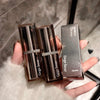 Two Gege bear lipsticks in open cases held by a hand on a textured surface.