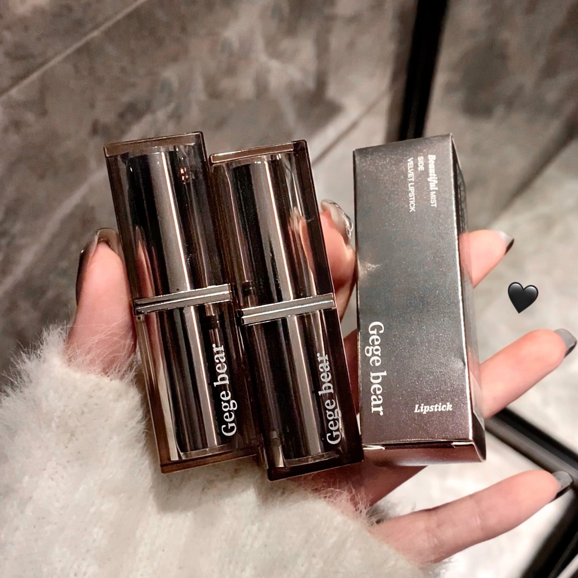 Two Gege bear lipsticks in open cases held by a hand on a textured surface.