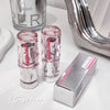 Two pink lip glosses and their packaging on a white surface with a mirror in the background.