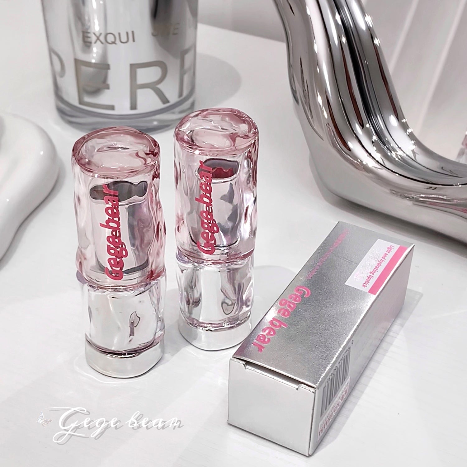 Two pink lip glosses and their packaging on a white surface with a mirror in the background.