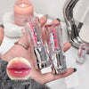 Two lip glosses held in a hand with a candle and mirror in the background