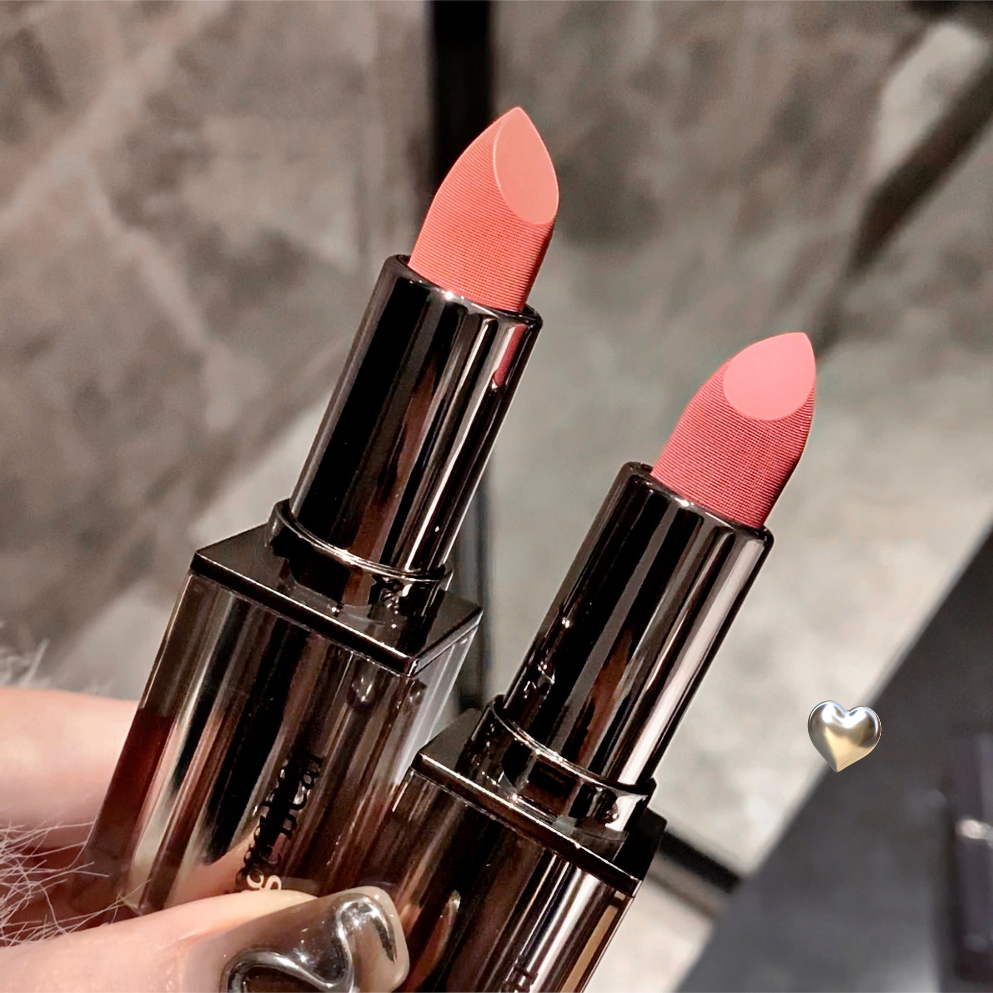 Two lipsticks with pink shades held by a hand against a neutral background