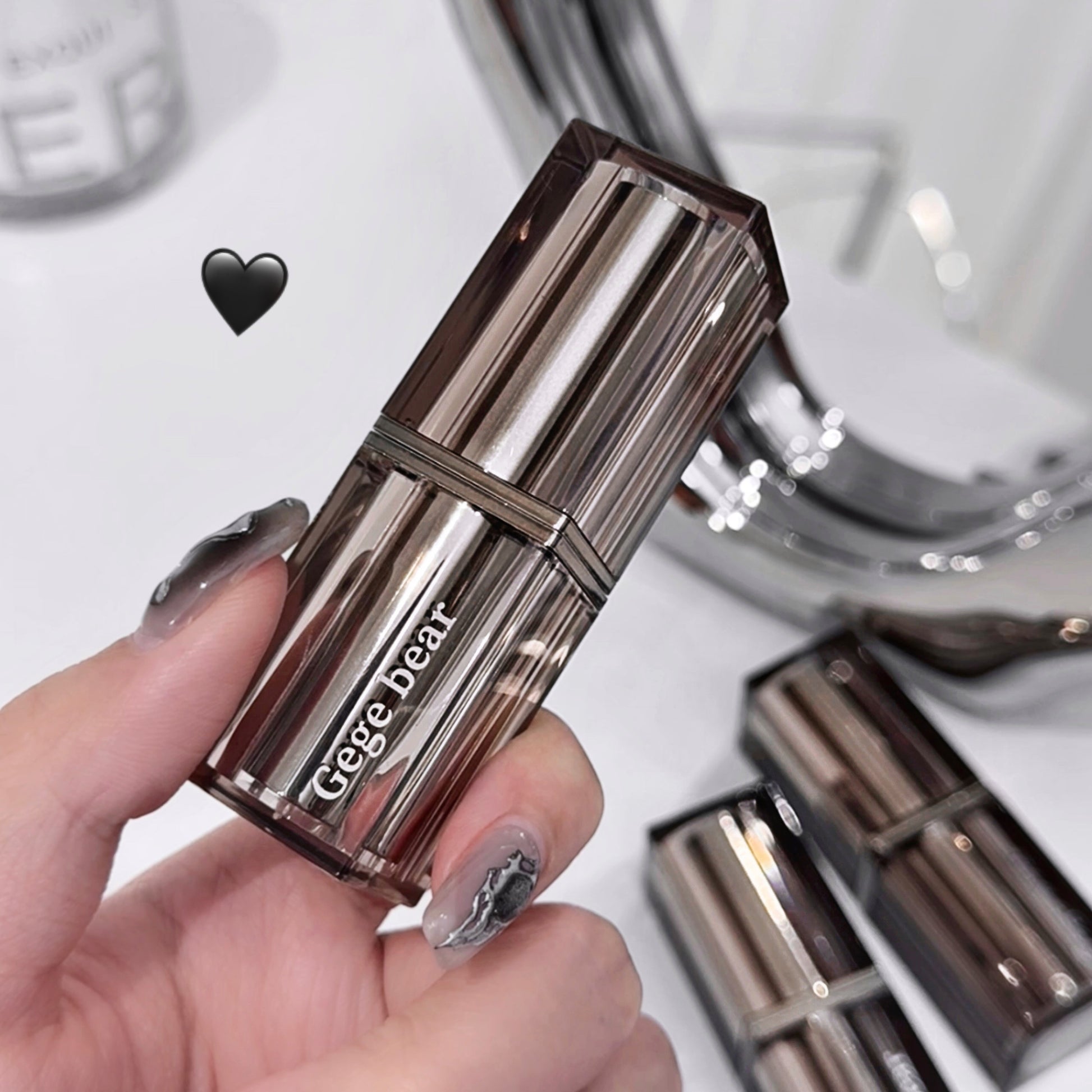 Hand holding a metallic lipstick with 'gege bear' branding, blurred background