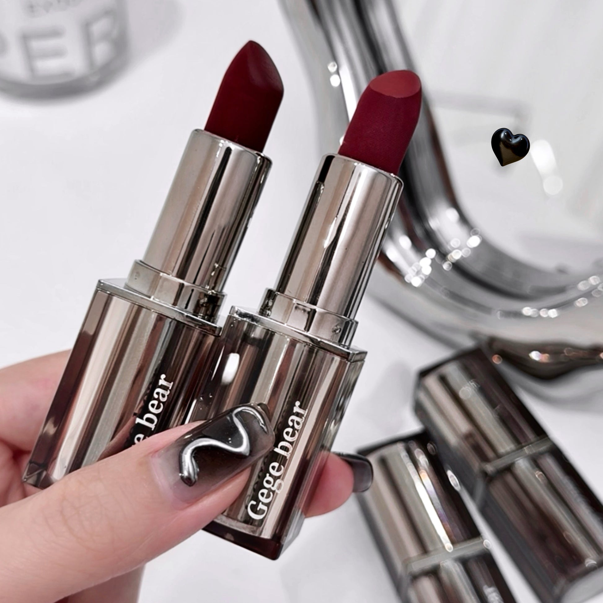 Two red lipsticks with silver packaging held by a hand, with a blurred background.