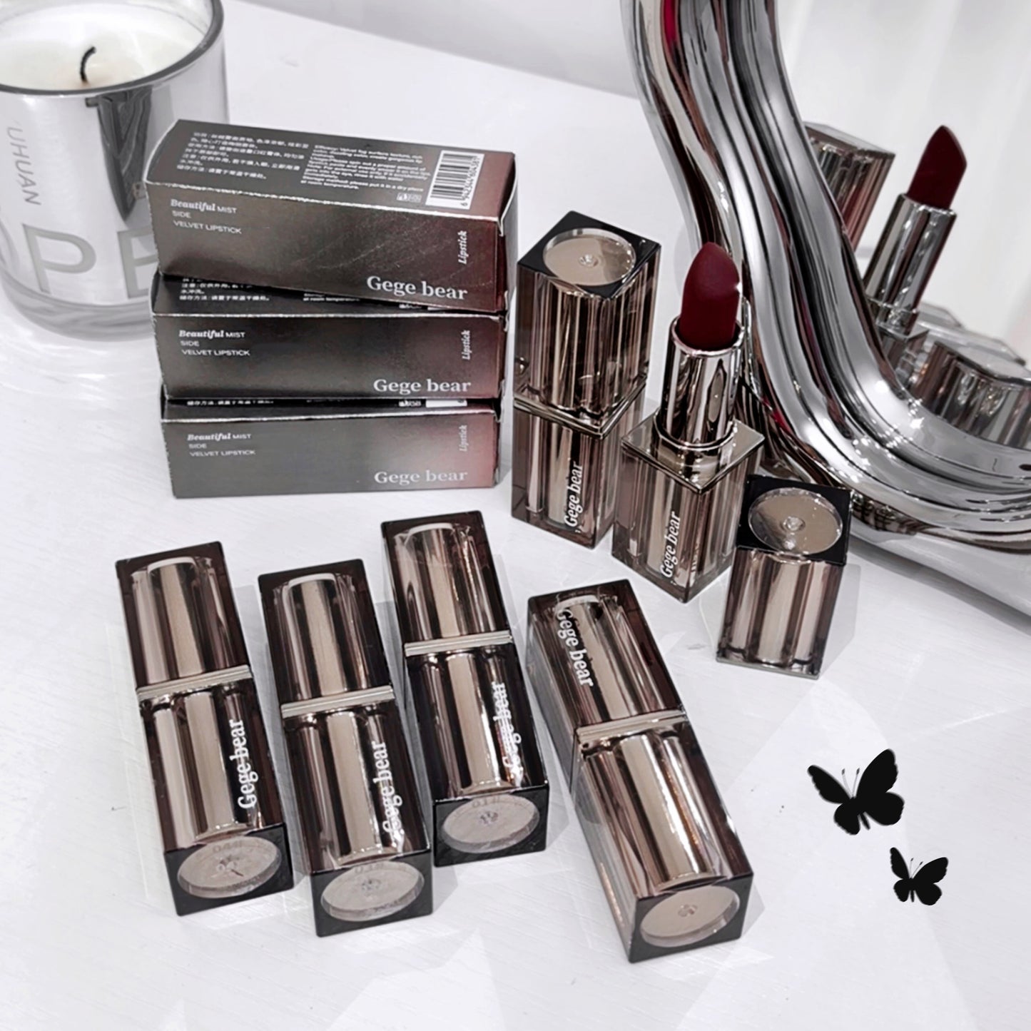 Collection of Gege bear lipsticks and packaging on a white surface with a mirror and candle in the background.