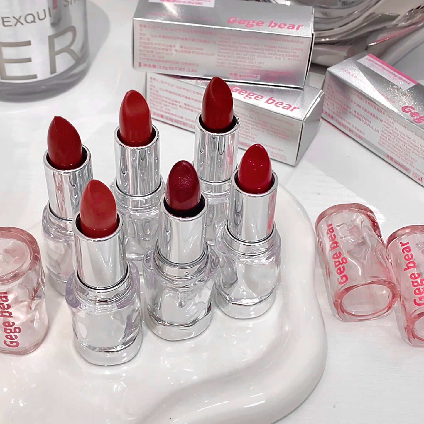 Red lipsticks with clear casings on a white surface, surrounded by 'Gee Bear' boxes.