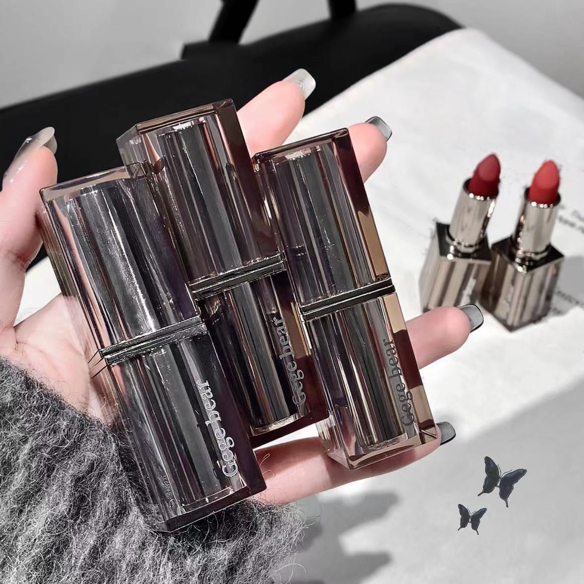 Close-up of three open lipsticks with visible brand name, held by a hand.