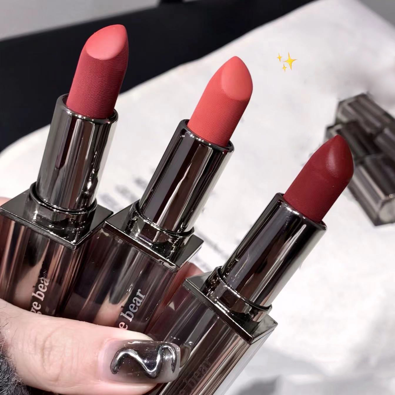 Three lipsticks of different shades held by a hand on a white background