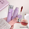 Purple lip gloss with a bow design held by a hand, with a close-up of lips at the bottom right corner.
