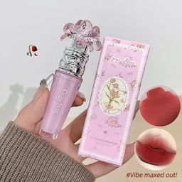 Pink lip gloss with decorative cap held by a hand, next to its packaging and color swatches.