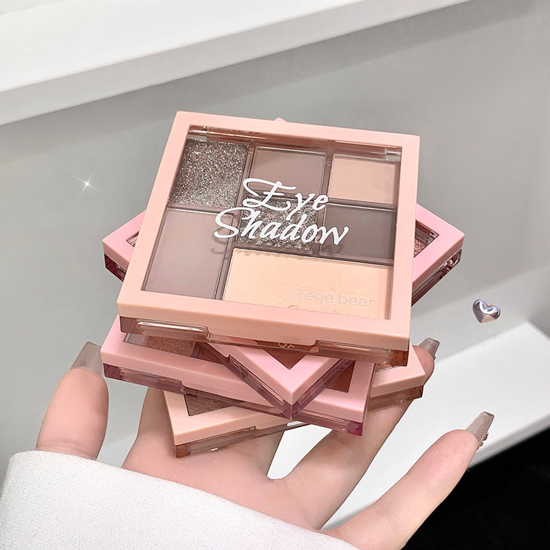 Hand holding a pink eyeshadow palette with multiple shades on a neutral background