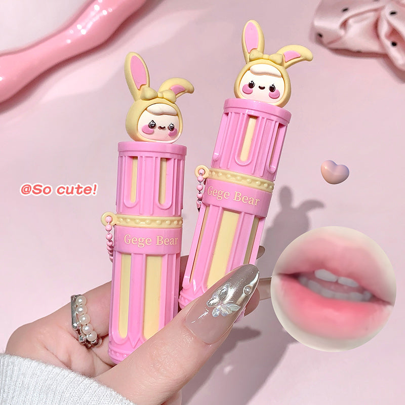 Two pink and yellow lip glosses with bunny designs held by a hand on a pink background.