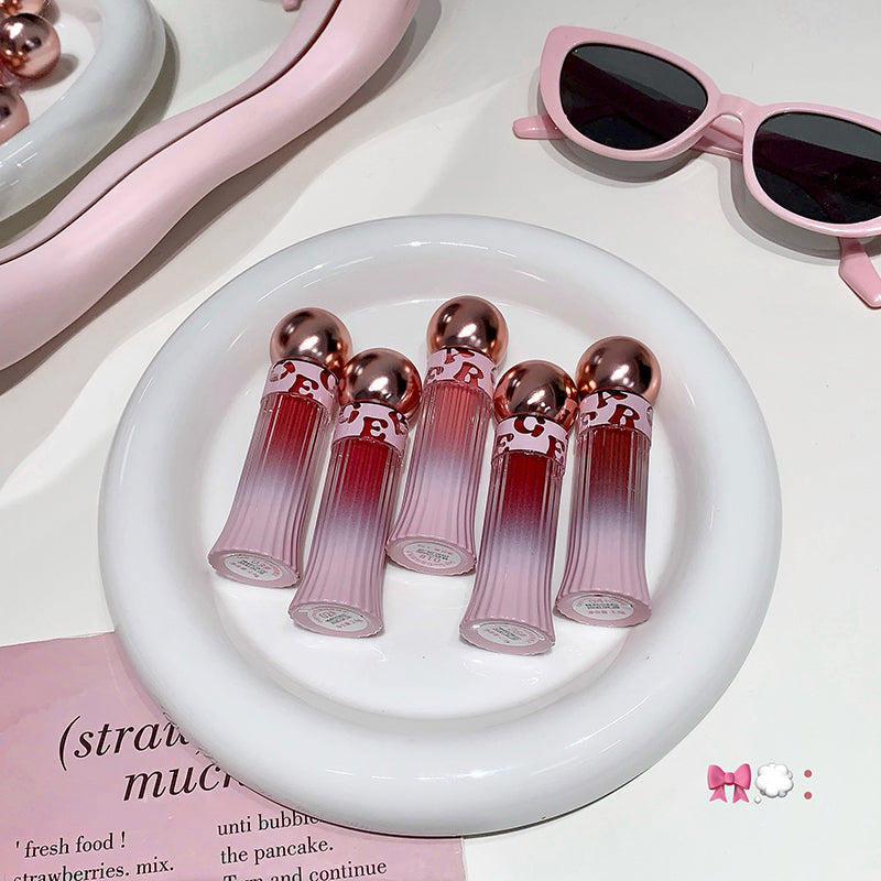 Set of pink lip glosses on a white plate with sunglasses in the background